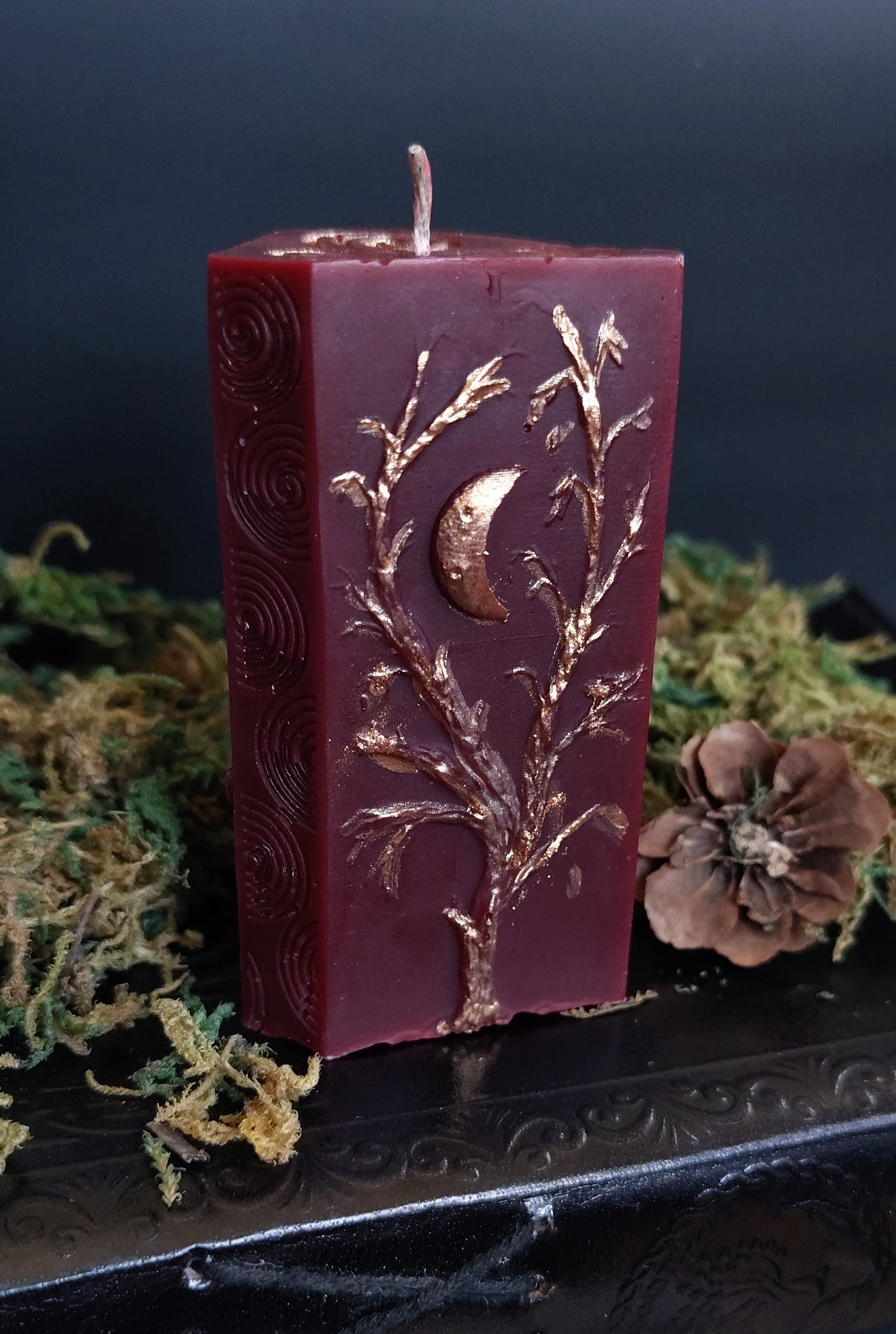 Sculptural candle with three apple tree carvings and a Triskele symbol, bronze‑detailed, handmade in Sioux Falls, SD.