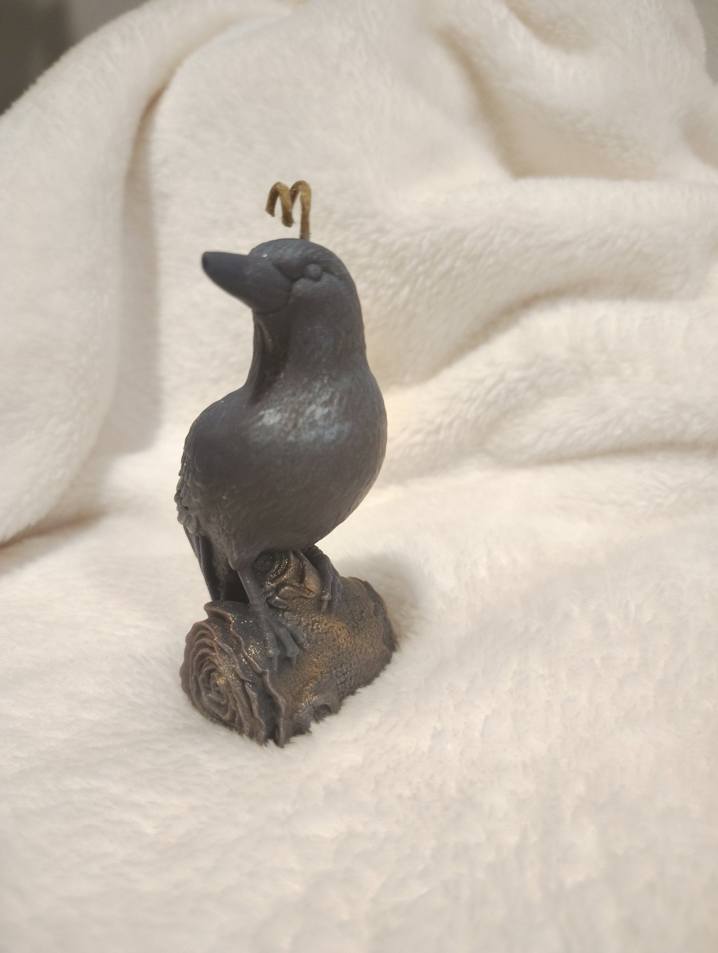 Small sculpture of a crow candle on a soft white background