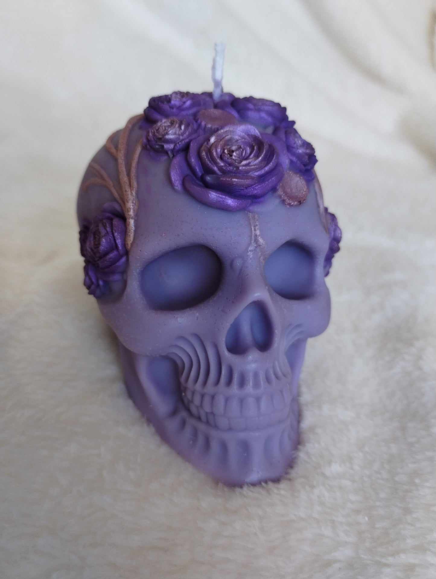 Purple skull-shaped candle with floral decorations on a beige surface