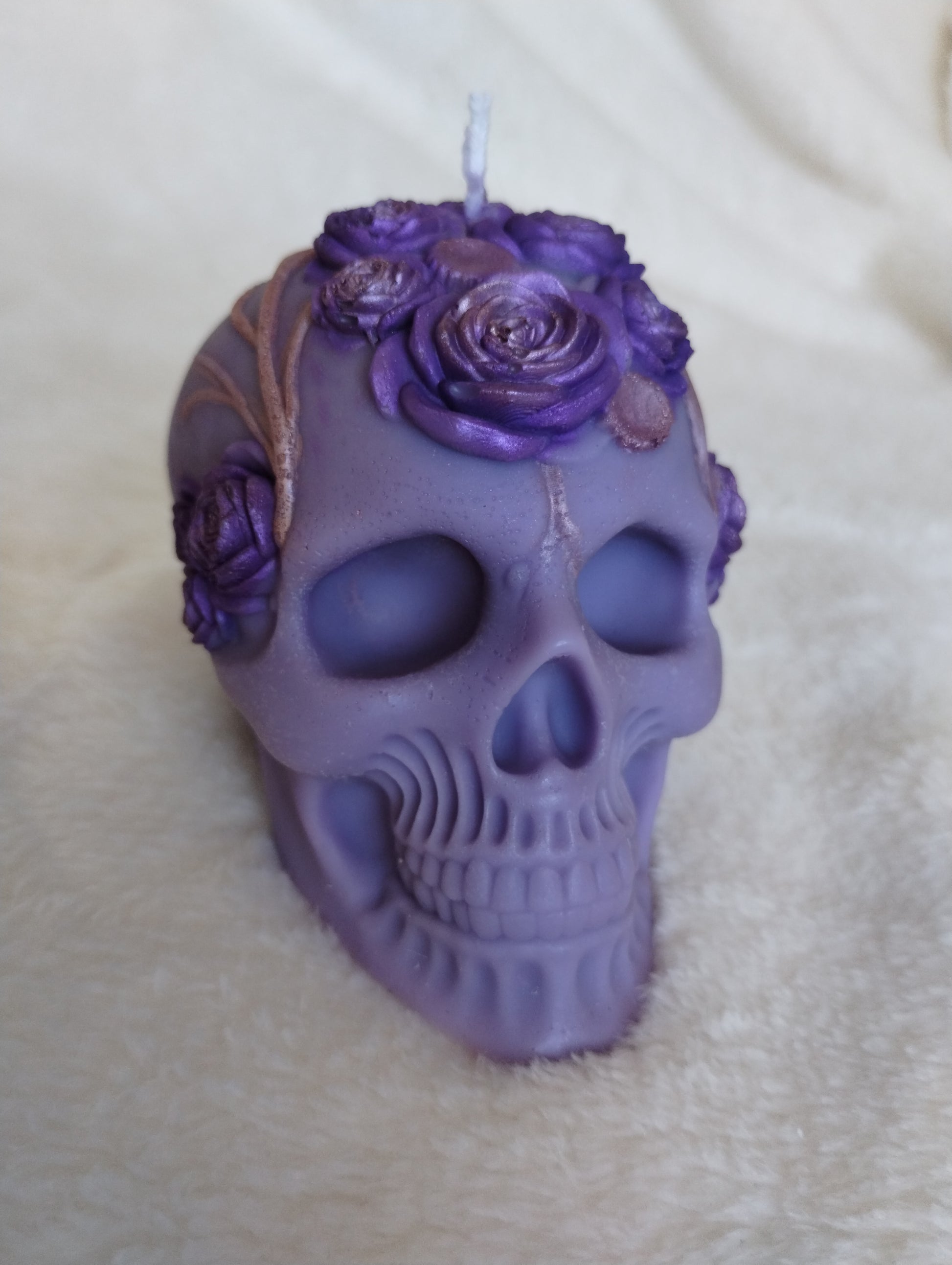 Purple skull-shaped candle with floral decorations on a beige surface