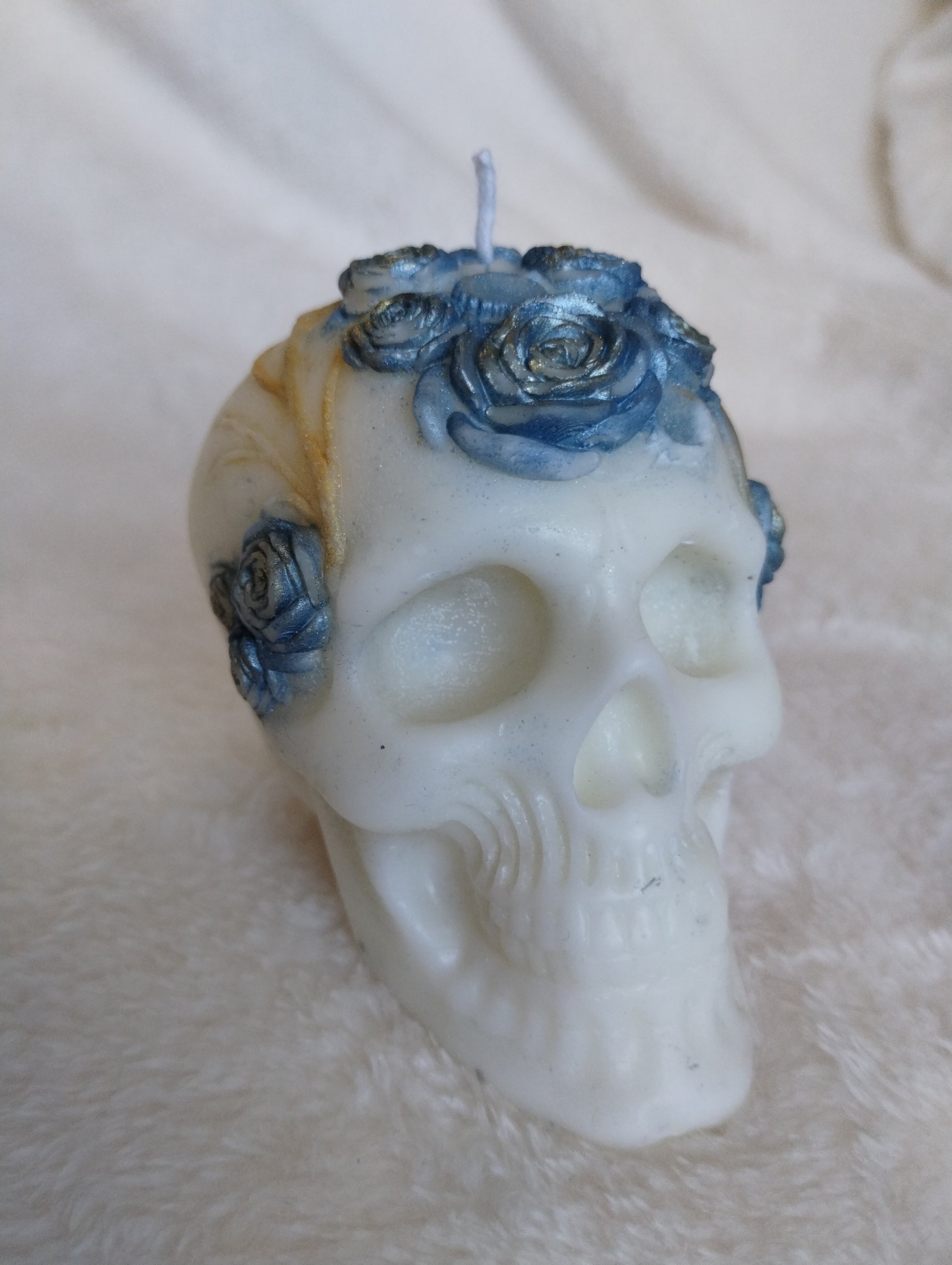 White skull-shaped candle with blue floral decorations on a beige surface