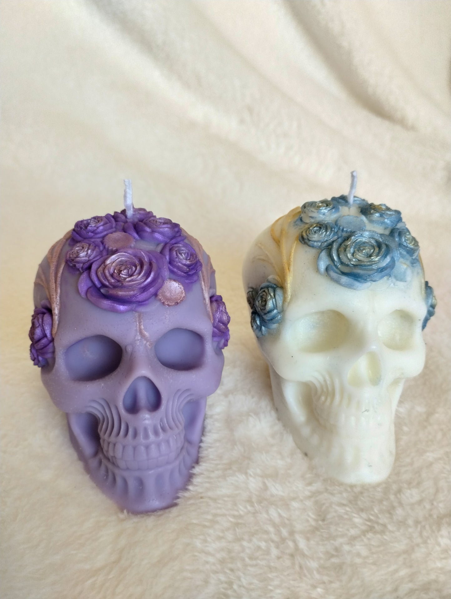 Two decorative skull candles with floral details on a beige fabric background