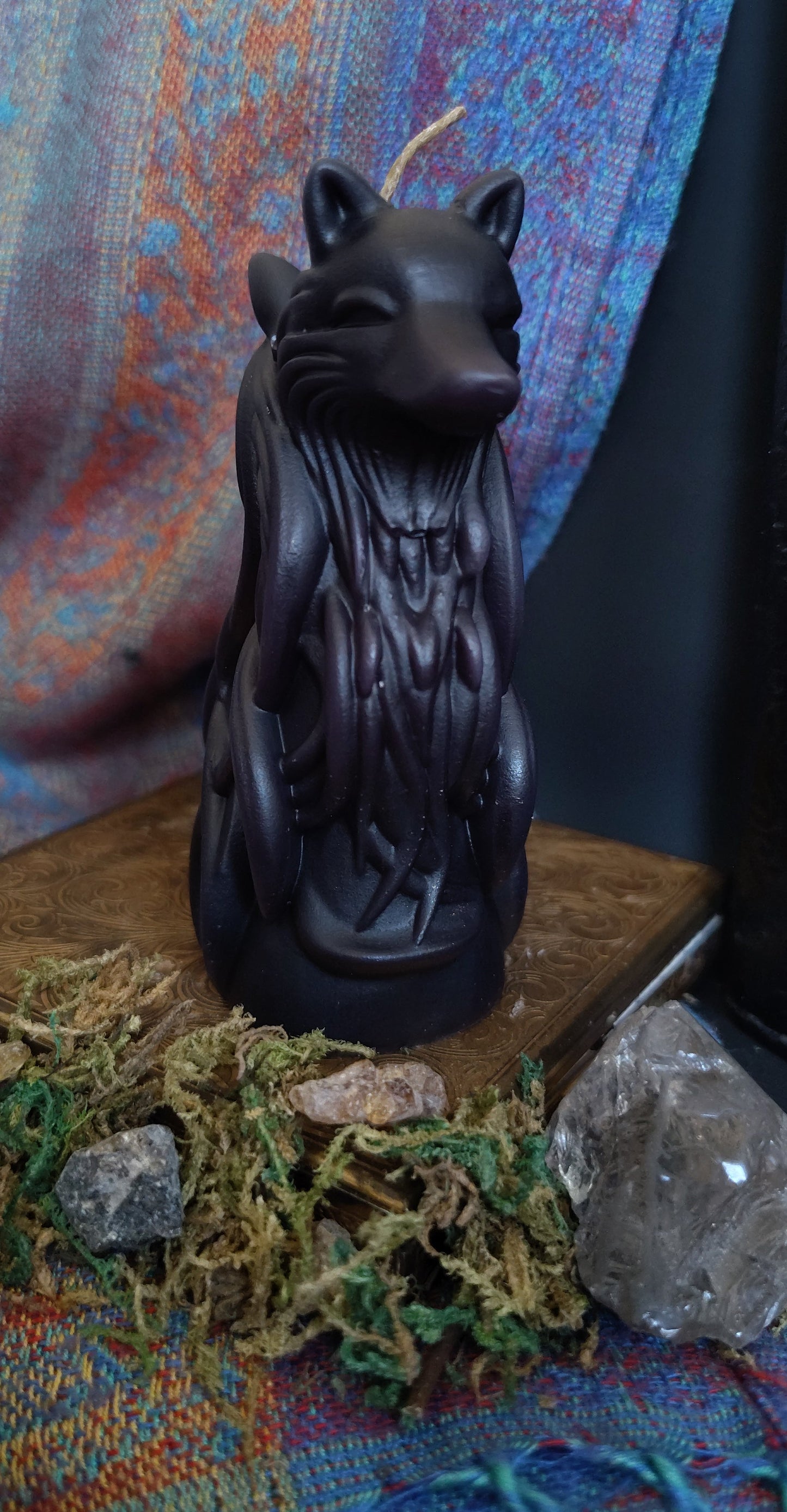 Black two headed wolf candle on a textured surface with crystals and stones
