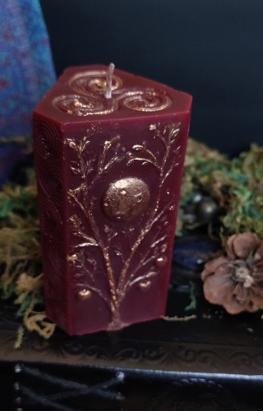 Sculptural candle with three apple tree carvings and a Triskele symbol, bronze‑detailed, handmade in Sioux Falls, SD.