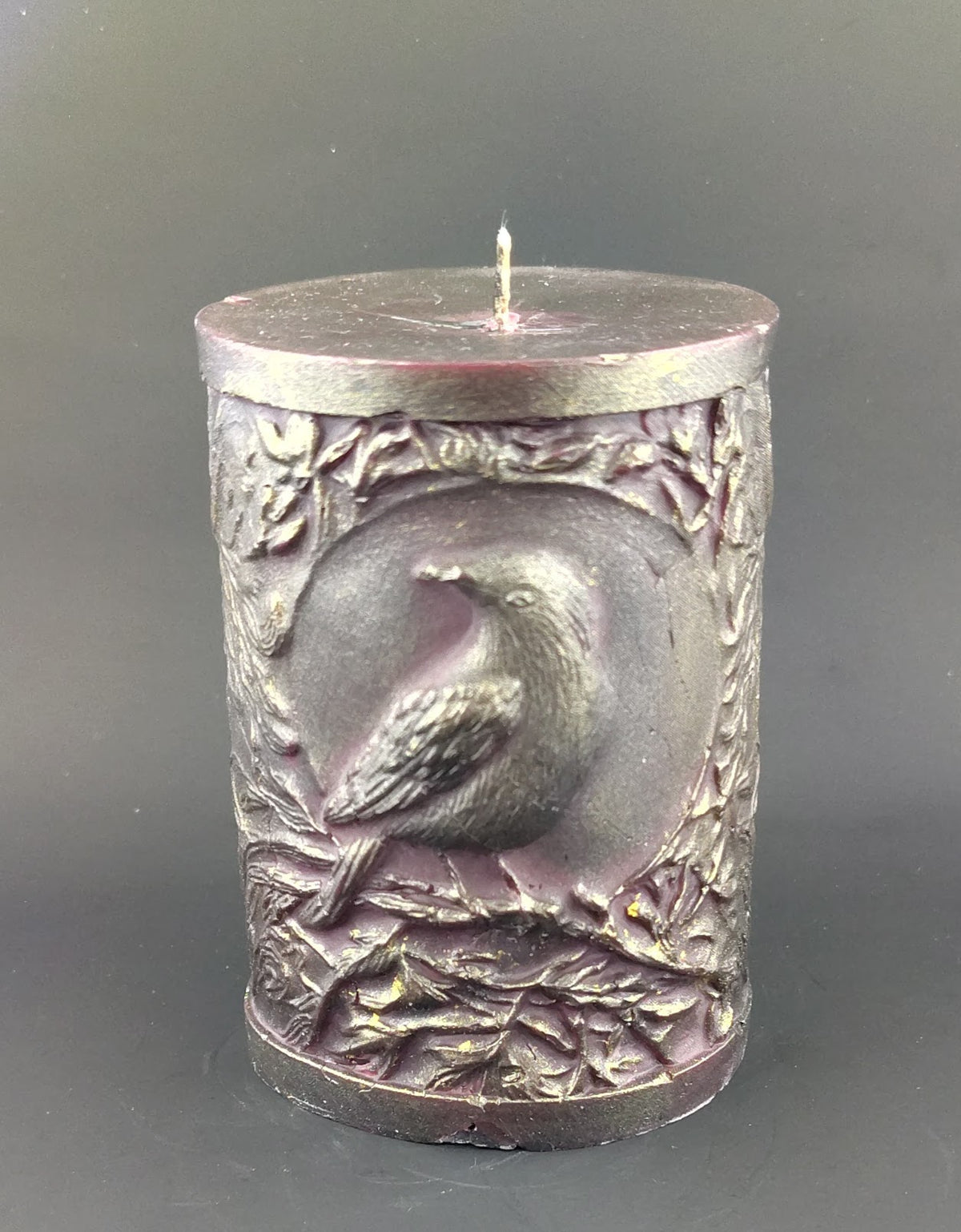 Deep red pillar candle with crow design and branches set on a dark background. 