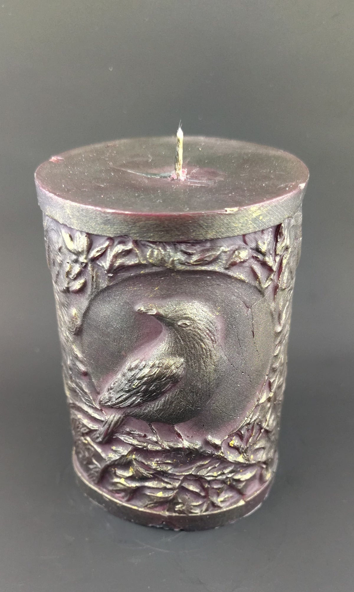 Deep red pillar candle with crow design and branches set on a dark background. 
