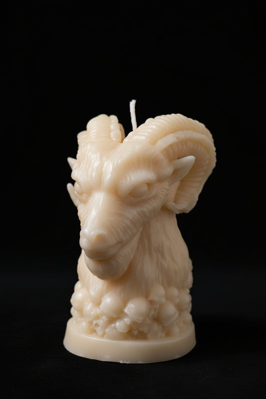 Rams head atop a pile of skulls candle with various items in the background. It looks like a workshop table photo. 
