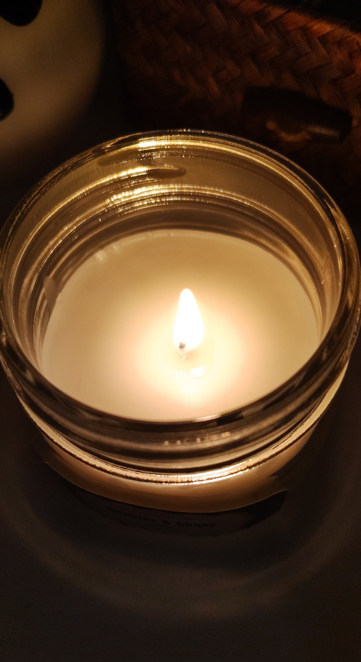 A lit jar candle with white wax in a clear glass container, photographed in warm, low lighting against a dark background.