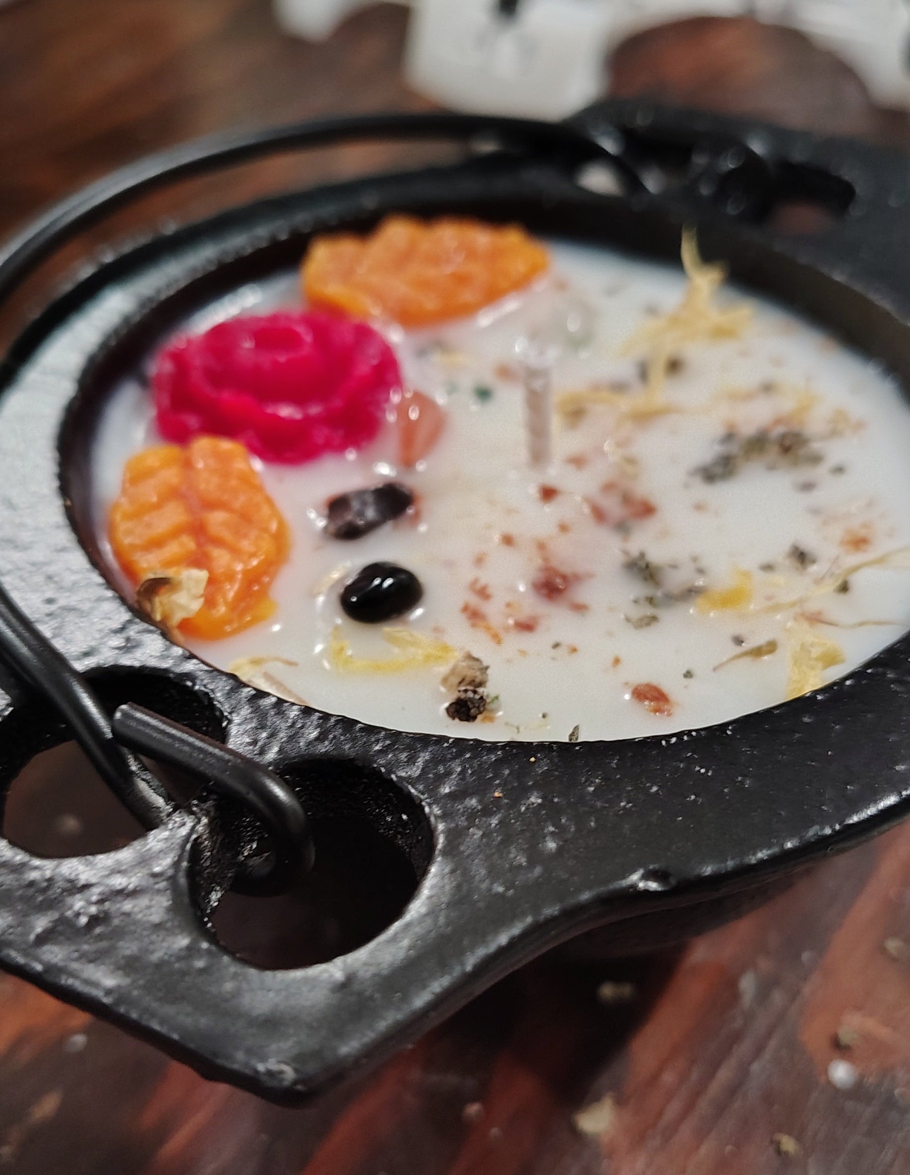A close-up shot of a black cast-iron cauldron filled with a candle scented and embellished, set on a wooden table.