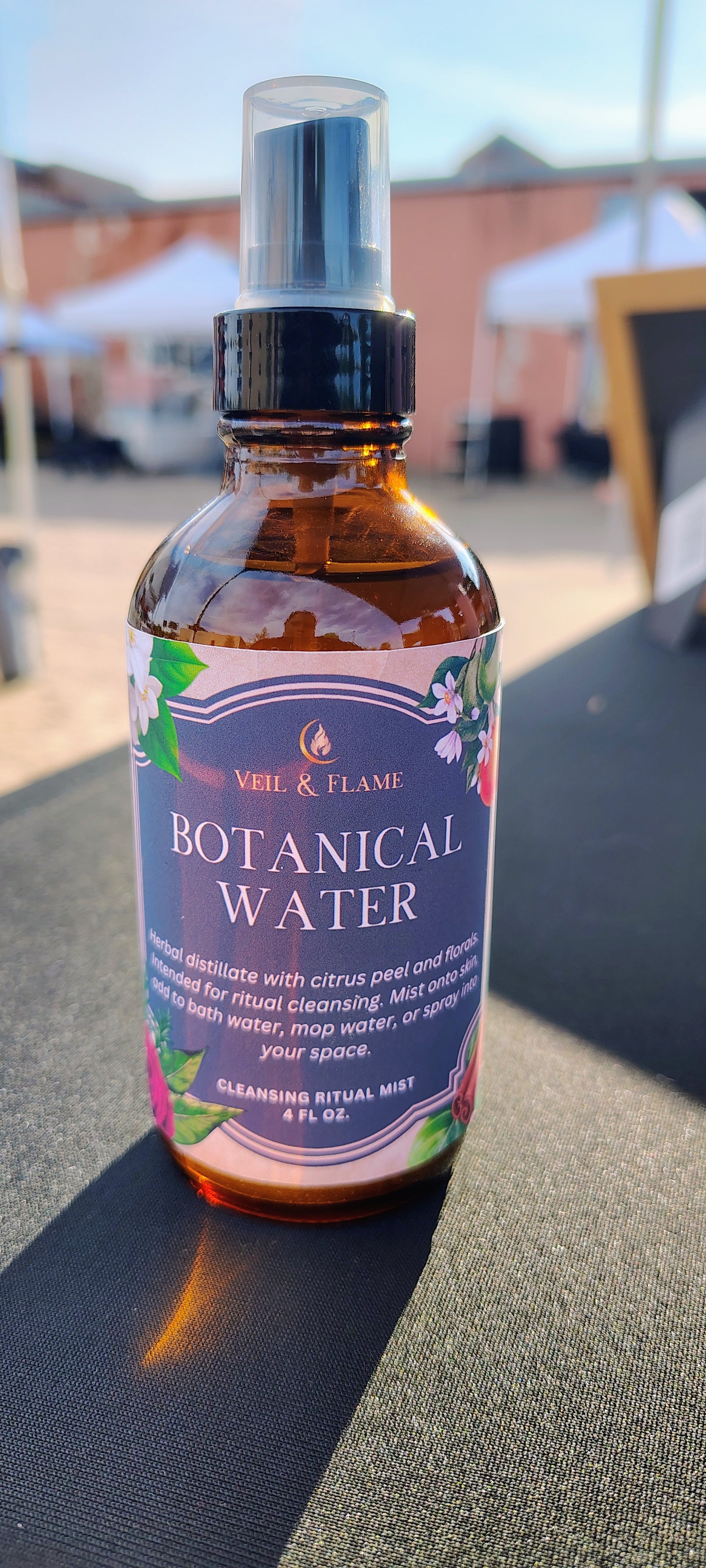 Bottle of Veil & Flame botanical water with a purple label on a black surface.