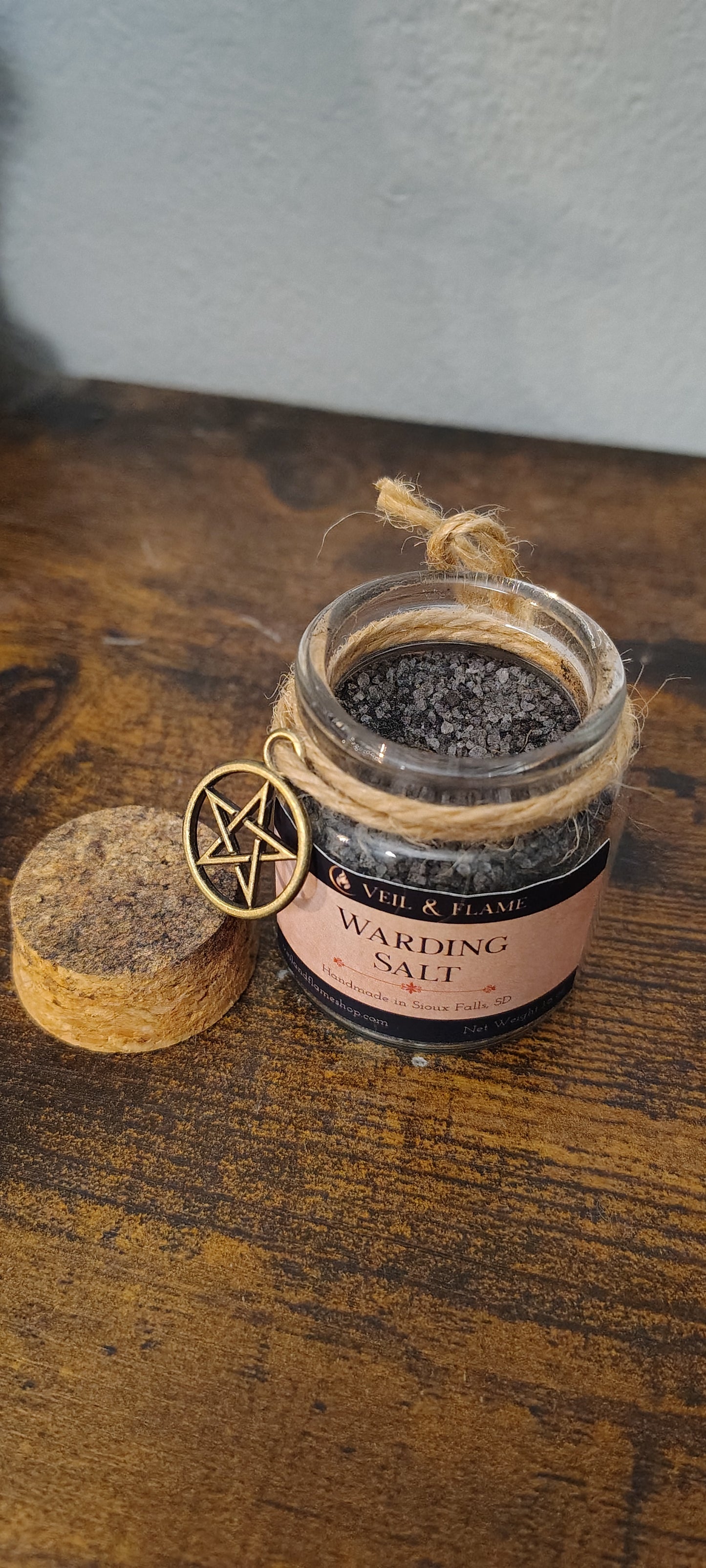 Jar of black salt with a pentagram charm on a wooden surface