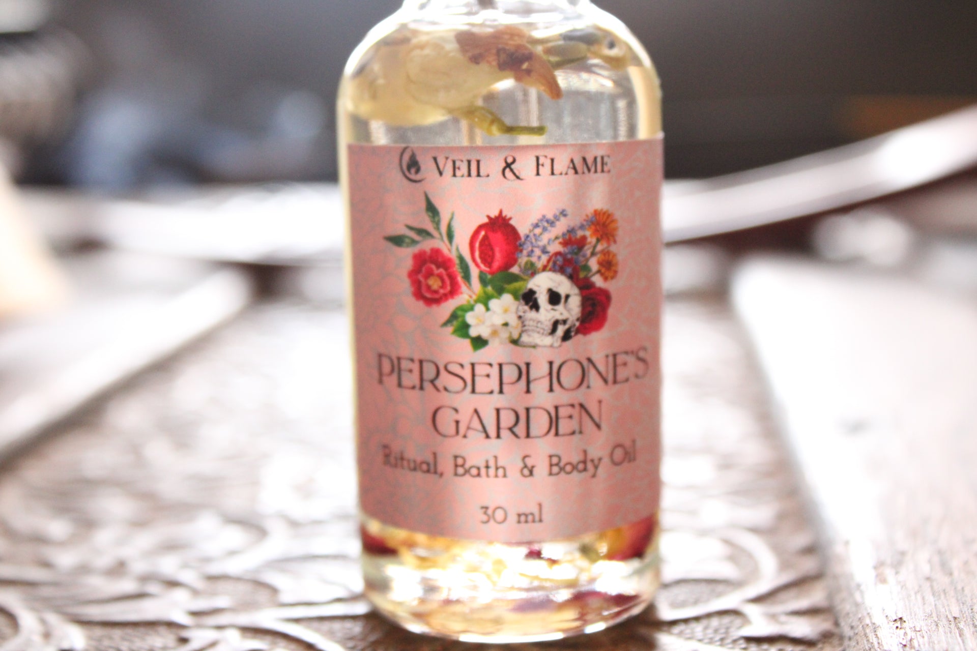 Bottle of 'Persephone's Garden' bath and body oil with floral label on a wooden surface.